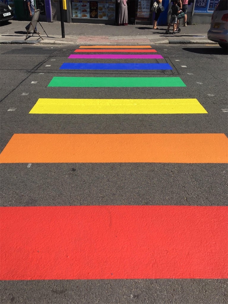 A pedestrian crossing where all of the white stripes have been painted with all the colours of the rainbow.